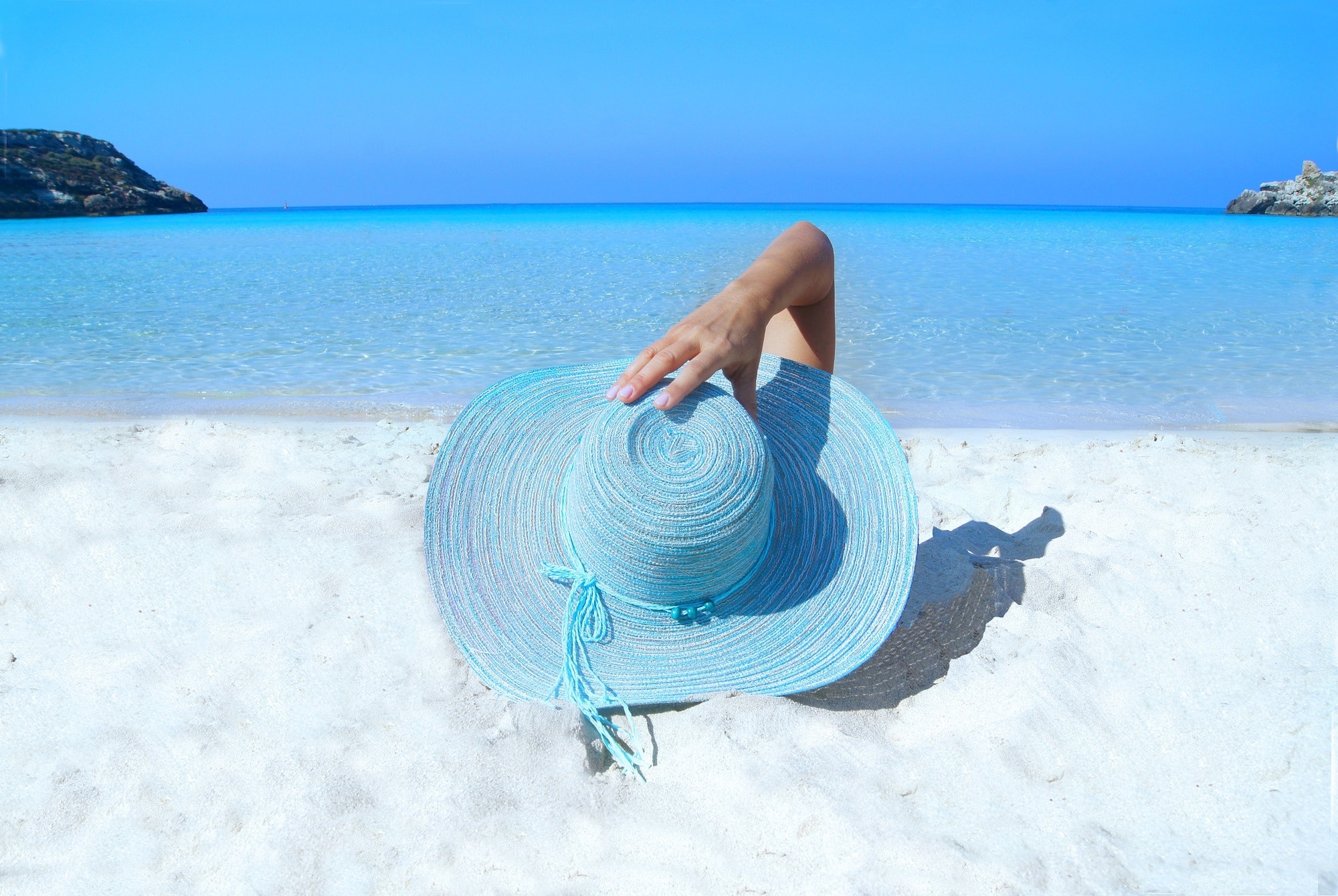 Kobieta leżąca na plaży z wielkim niebieskim kapeluszem, który przysłania ją całą