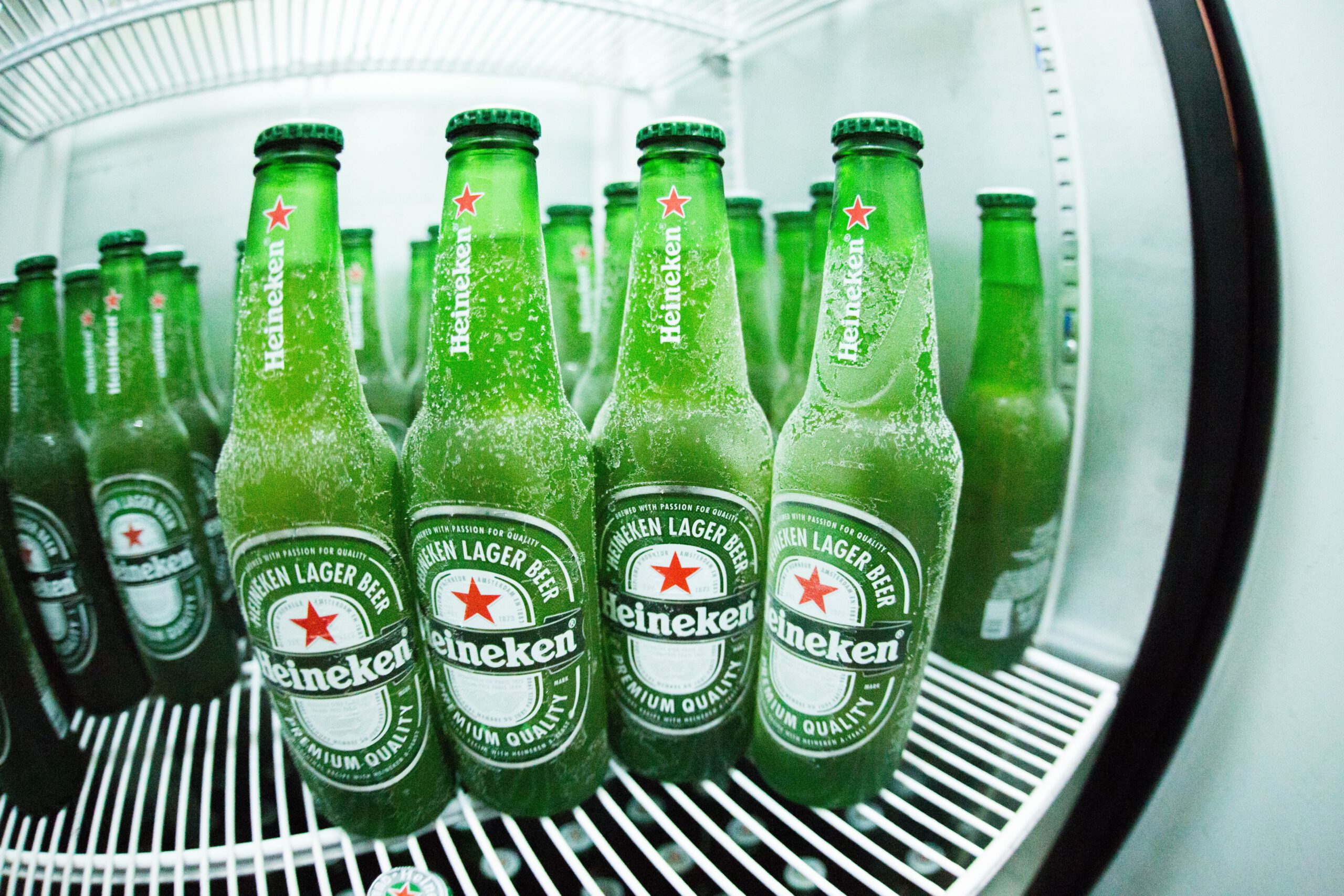 Zielone butelki z popularnym piwem, stojące w lodówce w sklepie monopolowym